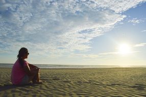 Woman sitting on a sand and looking at the sun