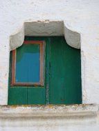 closed window with green shutters on white stone facade