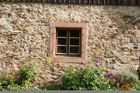 Small window on the stone wall and flowers