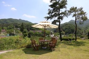 landscape of summer table with parasol on the law and mountains