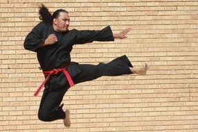 a man with red belt and black suit demonstrating a kick