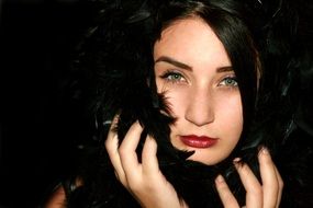 Portrait of green-eyed woman with black hair decorated black feathers