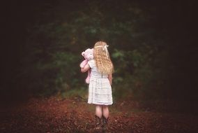 a view from the back on the little girl with pink teddy bear in the hands outdoors