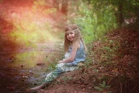 Happy baby girl sitting in a forest near the water