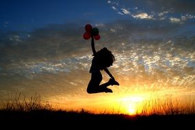 girl with balloons in hands jumped on the sunset background