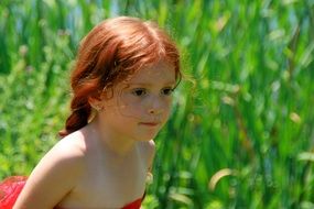 girlie with red hair on a background the stems of green grass