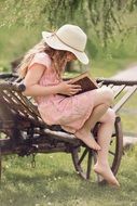 young girl in hat reading book among the plants