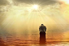 man stands in the ocean under the rays of the sun