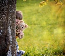 girl hiding behind tree with teddy