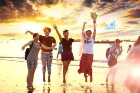 girls jumping on wet sand at sunset