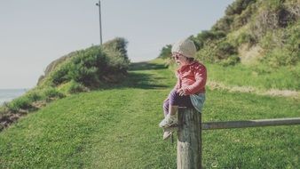 little girl in a red jacket and sunglasses sits on a fence