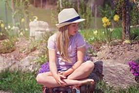 blond girl in the hat sitting in the garden