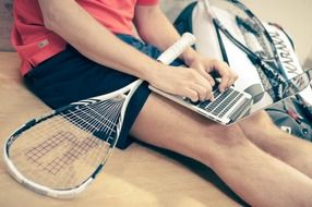 tennis racket and laptop on sitting manâs legs