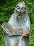 sculpture of an old man with a book near a green bush