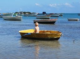 boy with an oar in a yellow boat on the background of sailboats