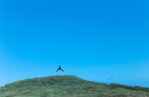 man jumping on green hill top at blue sky