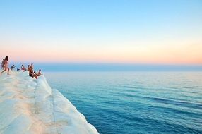 people on a white rock on the coast