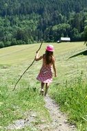 child girl walking witn stick green meadow