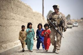 Afghan children and an American soldier walk along the road