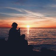 sitting woman with smartphone silhouette at sunset seascape