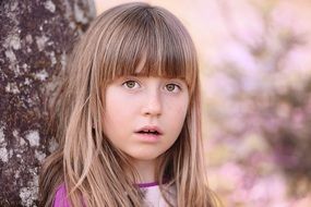 Young blonde girl leaning on the wood at blurred background with colorful plants