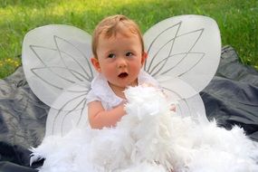 toddler in a white angel costume with wings playing with feathers