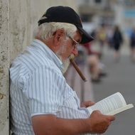 senior citizen with a cigar is reading a book