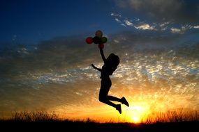 silhouette girl with balloons on the sunset background