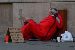 a homeless man lies in a red blanket near the house
