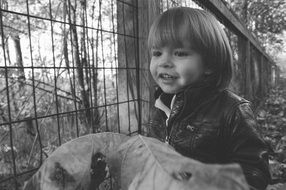 black and white photo of a charming child near a wire fence