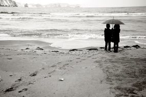 black and white photo of children under an umbrella near the sea