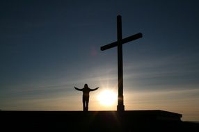 man and a symbol of Christianity on a background of sunrise