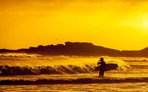 surfer stands near surfline at sunset