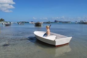 boy with a paddle in white boat on a background sailboats