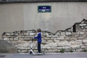 a child on a scooter stands near a wall