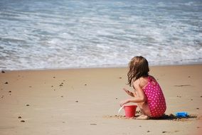 little girl plays on the sand at the beach