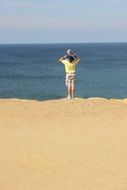 father carries baby on his shoulders at the beach