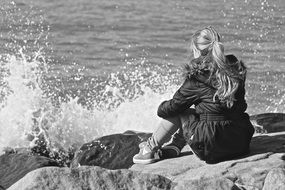 Black and white photo of lonely girl sitting on a rocky shore