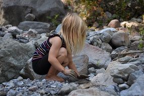 girl with white hair plays on a rocky shore