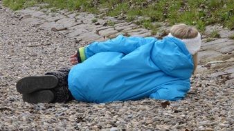 child girl lays on her side on pebbles, back view