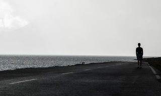 silhouette of a man walking along the sidewalk along the ocean