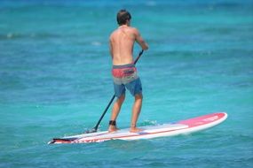 man in shorts with a paddle on a surfboard