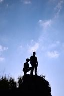 silhouette of guys on a high rock