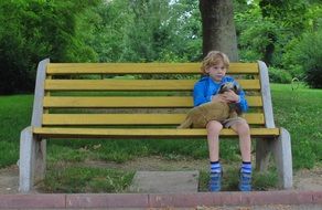 little boy with a dog on a park bench