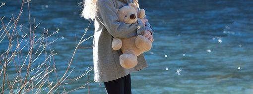 girl with a teddy bear in hands near the river