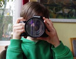 child holds camera near face with reflection in the lens