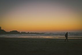 man is walking on the beach at sunset