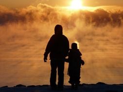 silhouette of a parent with a child on a background of fog at dawn