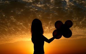 shadowed silhouette of a girl with balloons in hands on sunset background