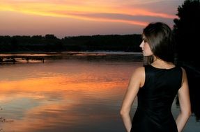 back view of a girl standing by the lake at sunset background